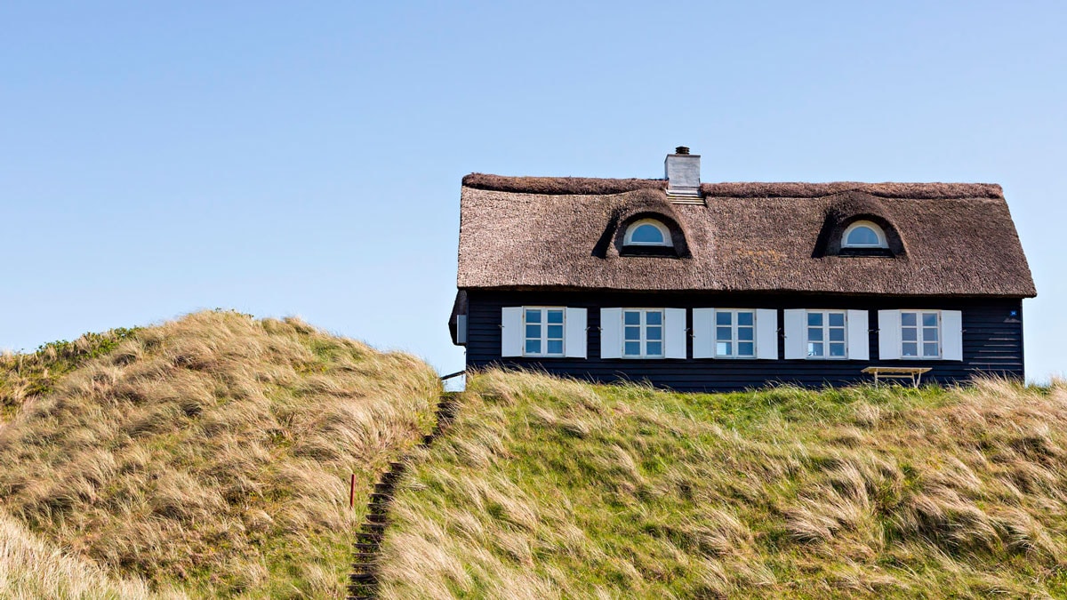 Sort sommerhus med stråtækt tag beliggende på klittop