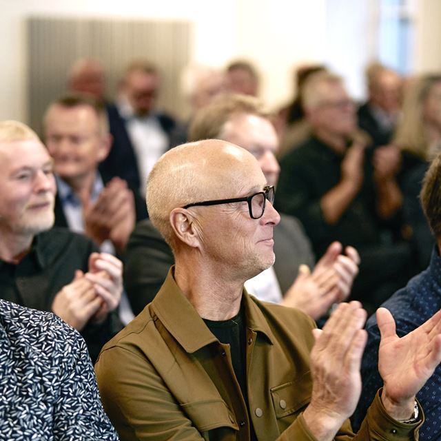 Mennesker sidder på stolerække og klapper