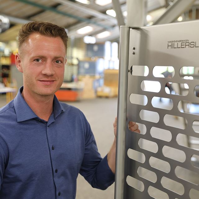 Jesper Krog Sørensen står foran en af maskinerne i fabrikshallen i Hillerslev